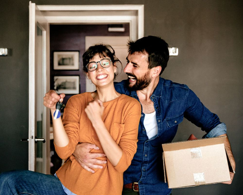 Ein junges Paar steht im neuen Eigenheim und freut sich.