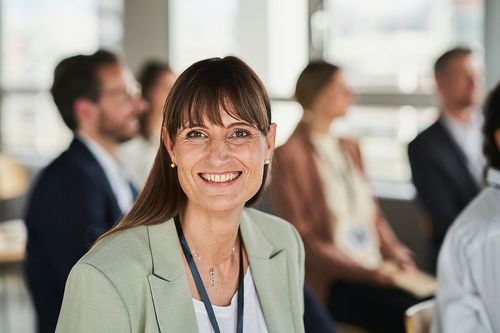 Weiterbildungsteilnehmerin bei einer Fachtagung lächelt freudig in die Kamera.