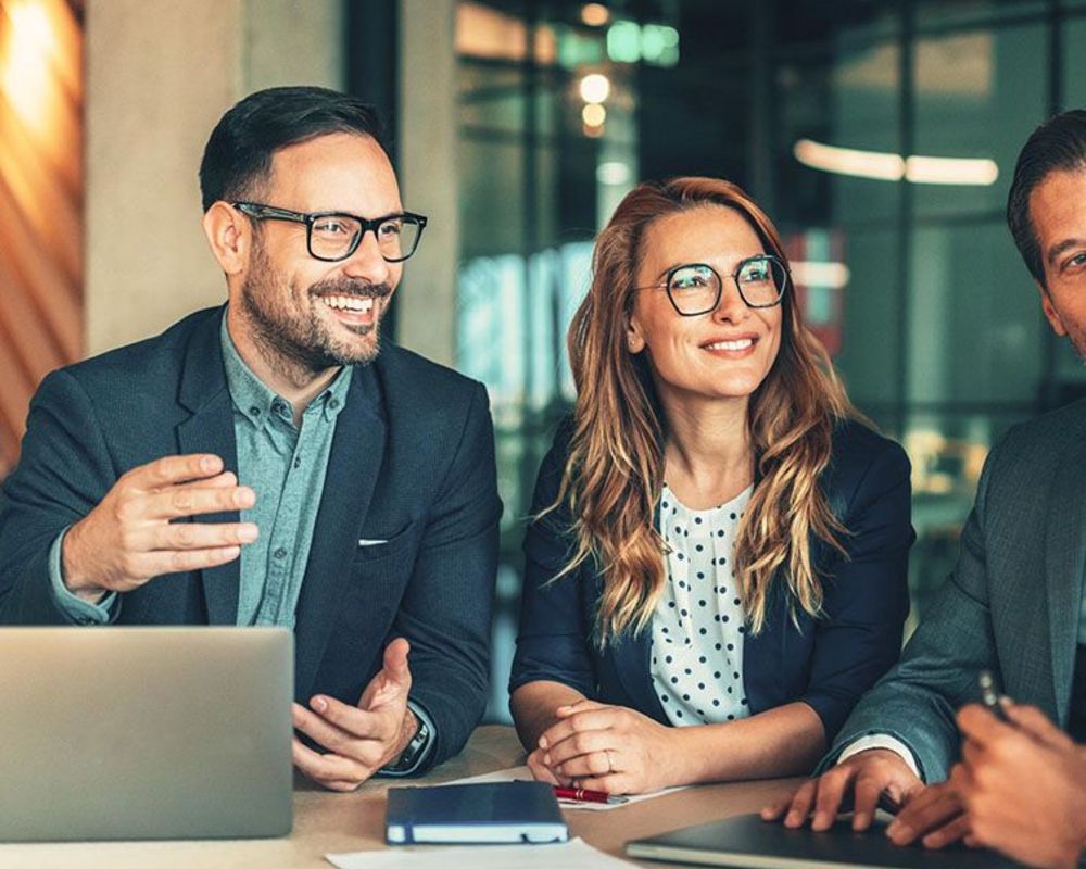 Mehrere Führungskräfte sitzen an einem Tisch für eine gemeinsame Besprechung. Vor ihnen liegen Laptops und Blöcke auf dem Tisch.