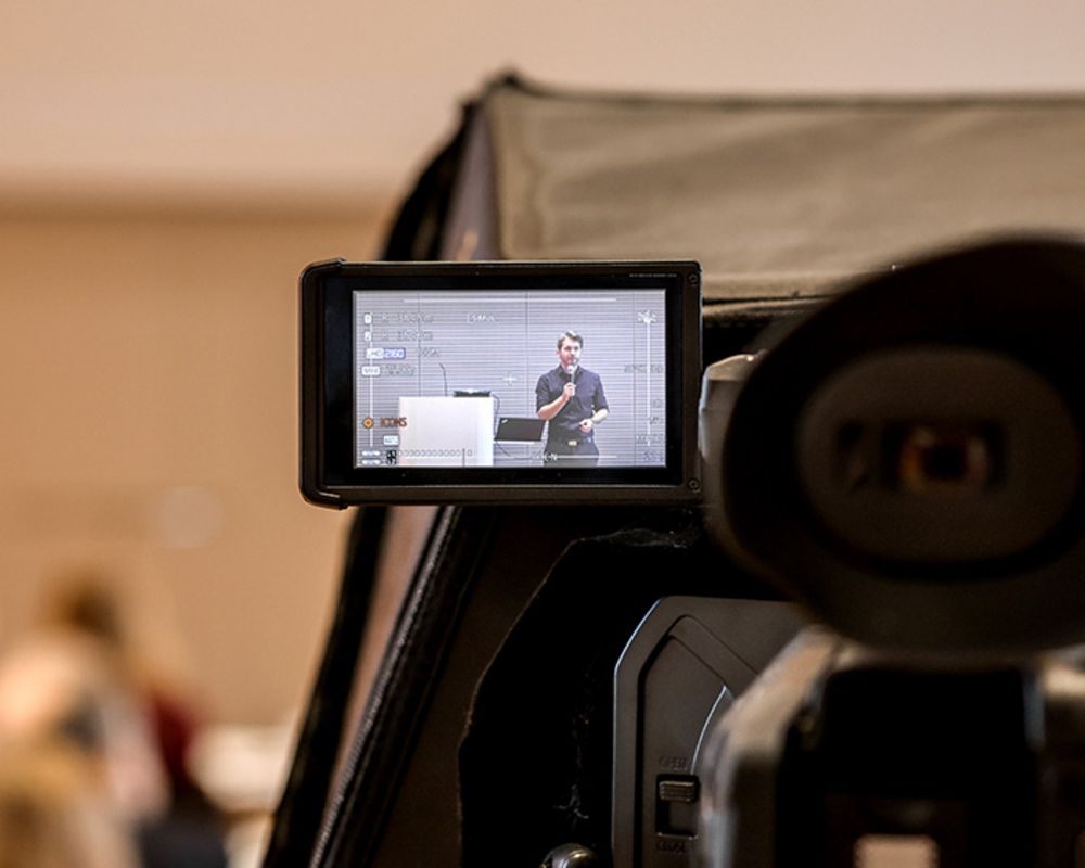 Auf dem Kamerabildschirm ist die Live-Aufzeichnung des Sprechenden einer Bildungsveranstaltung zu sehen, der vor den Seminarteilnehmenden spricht.