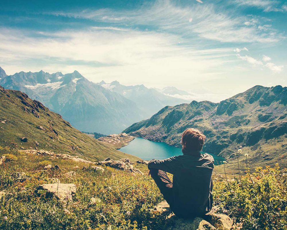 Ein Wanderer sitzt auf einem Berg und genießt die Aussicht über das Tal.