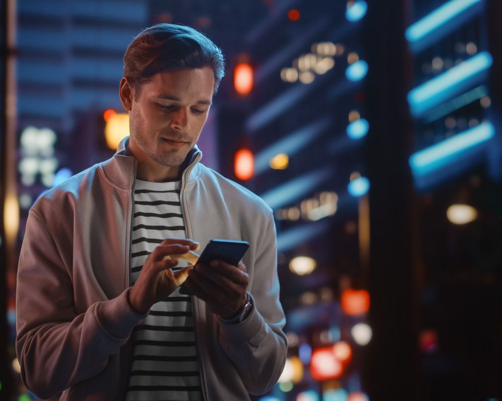 Junger Mann läuft abends durch die Stadt und nutzt die digitalen Angebote der Sparkasse über sein Mobiltelefon.