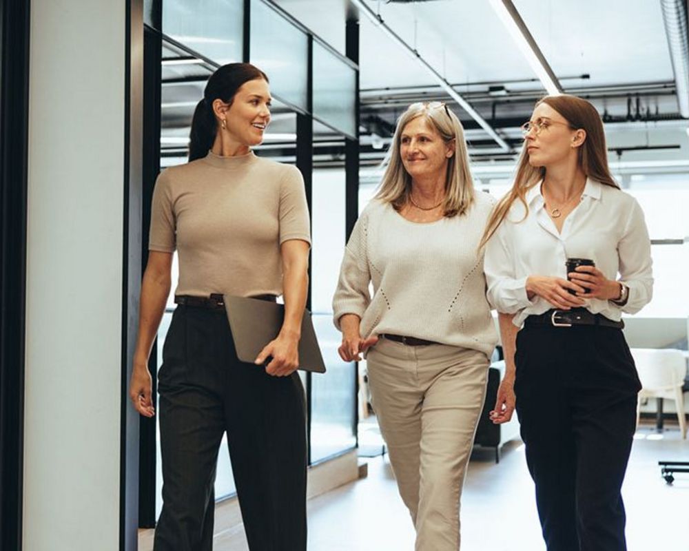 Eine Gruppe von drei Frauen laufen gemeinsam durch einen Flur auf dem Weg zu einer Veranstaltung zur Frauenförderung