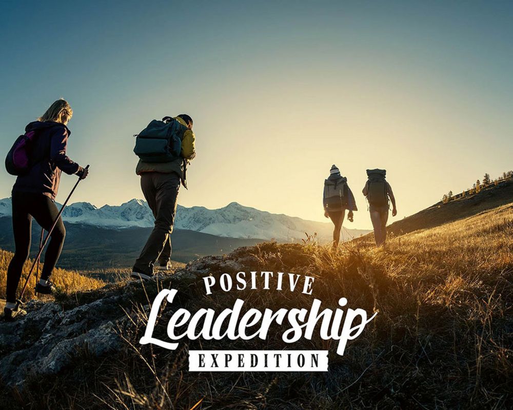 Wanderer auf einem Berg vor dem Sonnenaufgang. Im Vordergrund ist das Logo von Positive Leadership Expedition zu sehen.