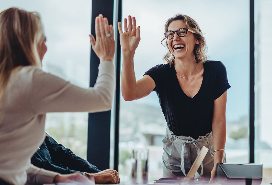 Zwei Frauen in einem Buero freuen sich und geben sich ein High Five