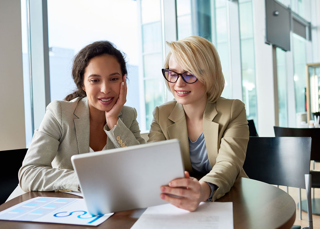 Zwei Frauen beraten sich zum Bildungsgutschein und schauen laechelnd auf ein Tablet
